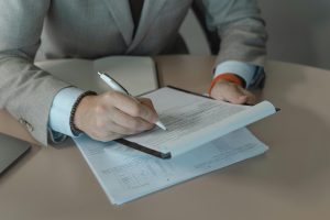 Person in Gray Suit Holding White Pen and Document on a Clipboard